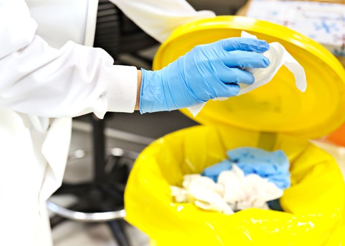 hospital staff throwing garbage in a yellow bin wearing blue nitrile gloves